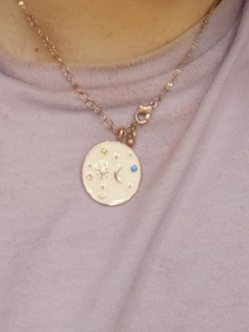 Golden necklace with moon-and-sun pendant against a pink shirt