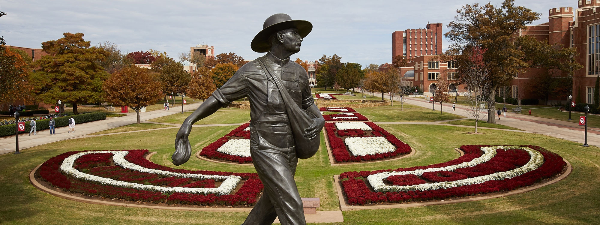 The Seed Sower statue in the foreground with white and crimson mums in flowerbeds in the background.