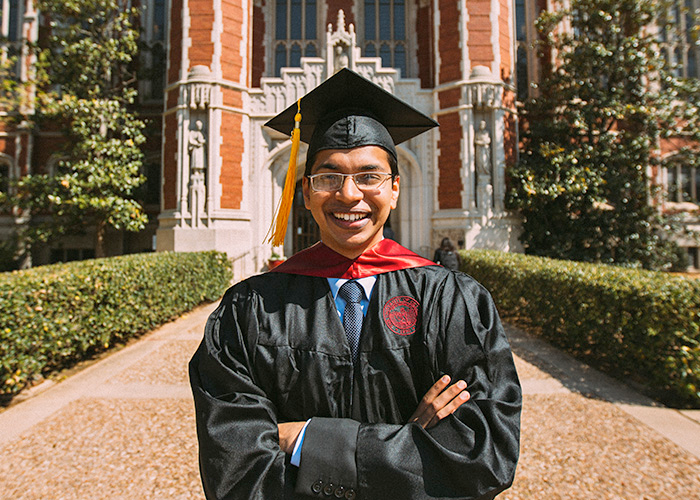 smiling student wearing cap and gown standing in front of Bizzell library
