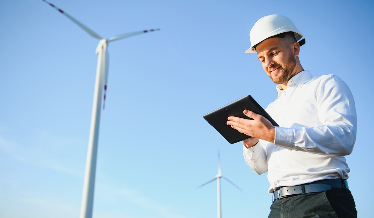 Energy executive checking data on his tablet while standing near a wind turbine