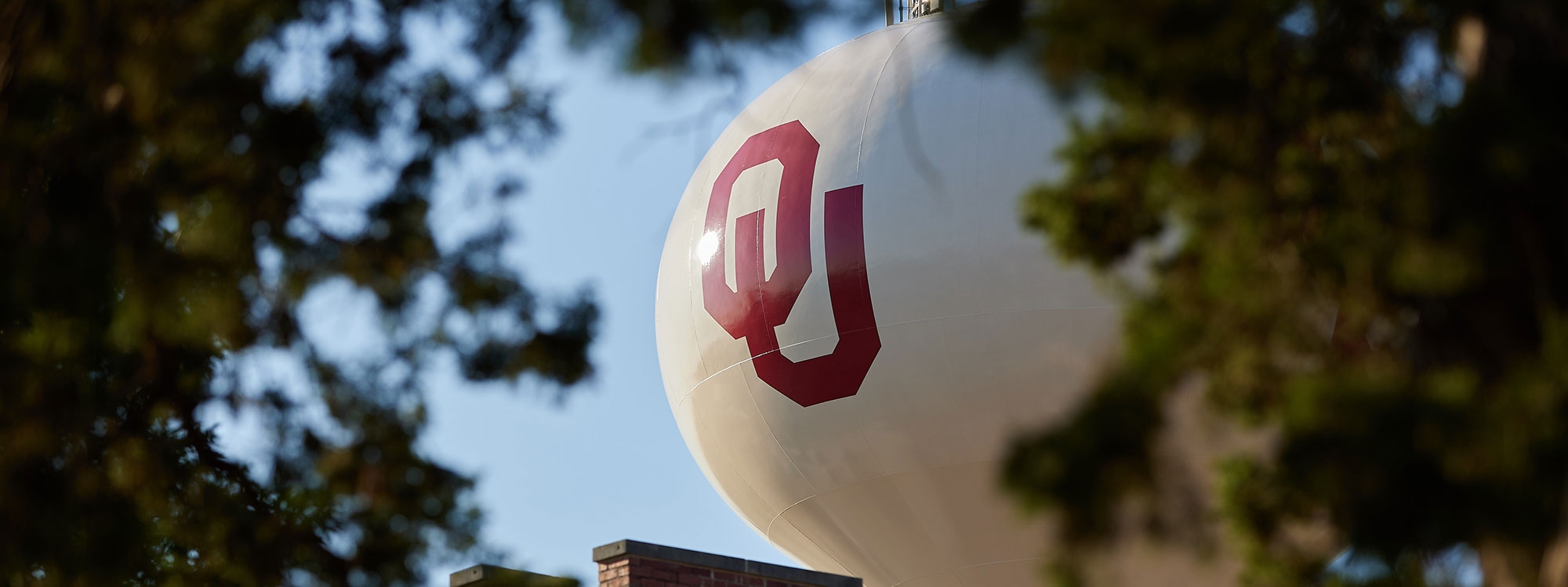 The OU water tower framed by trees and a blue sky.