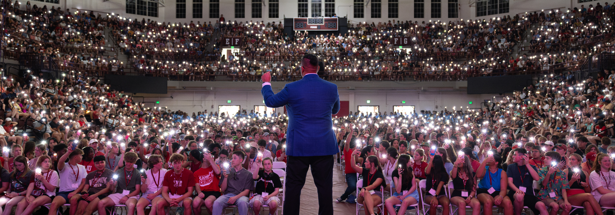 Campers in the stands holding up phone flashlights during Camp Crimson opening session.