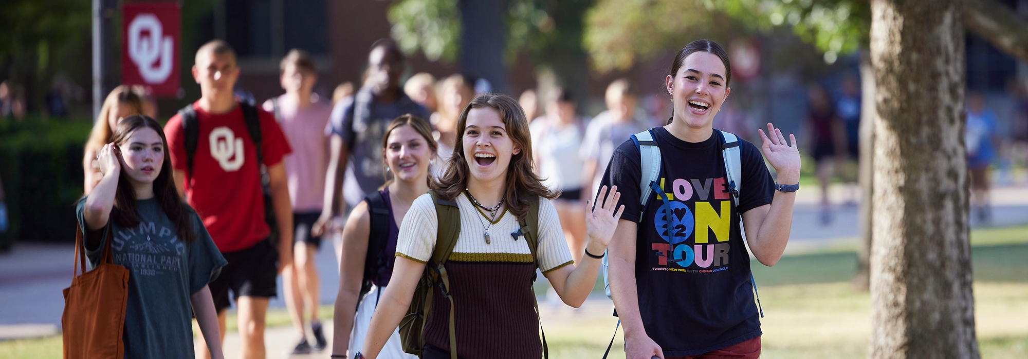 Students walking on campus at the University of Oklahoma and waving.