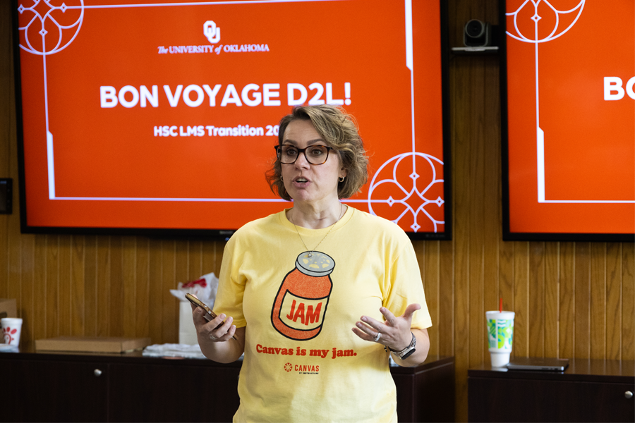 A woman speaking in front of a sign that says 'Bon Voyage D2L!'