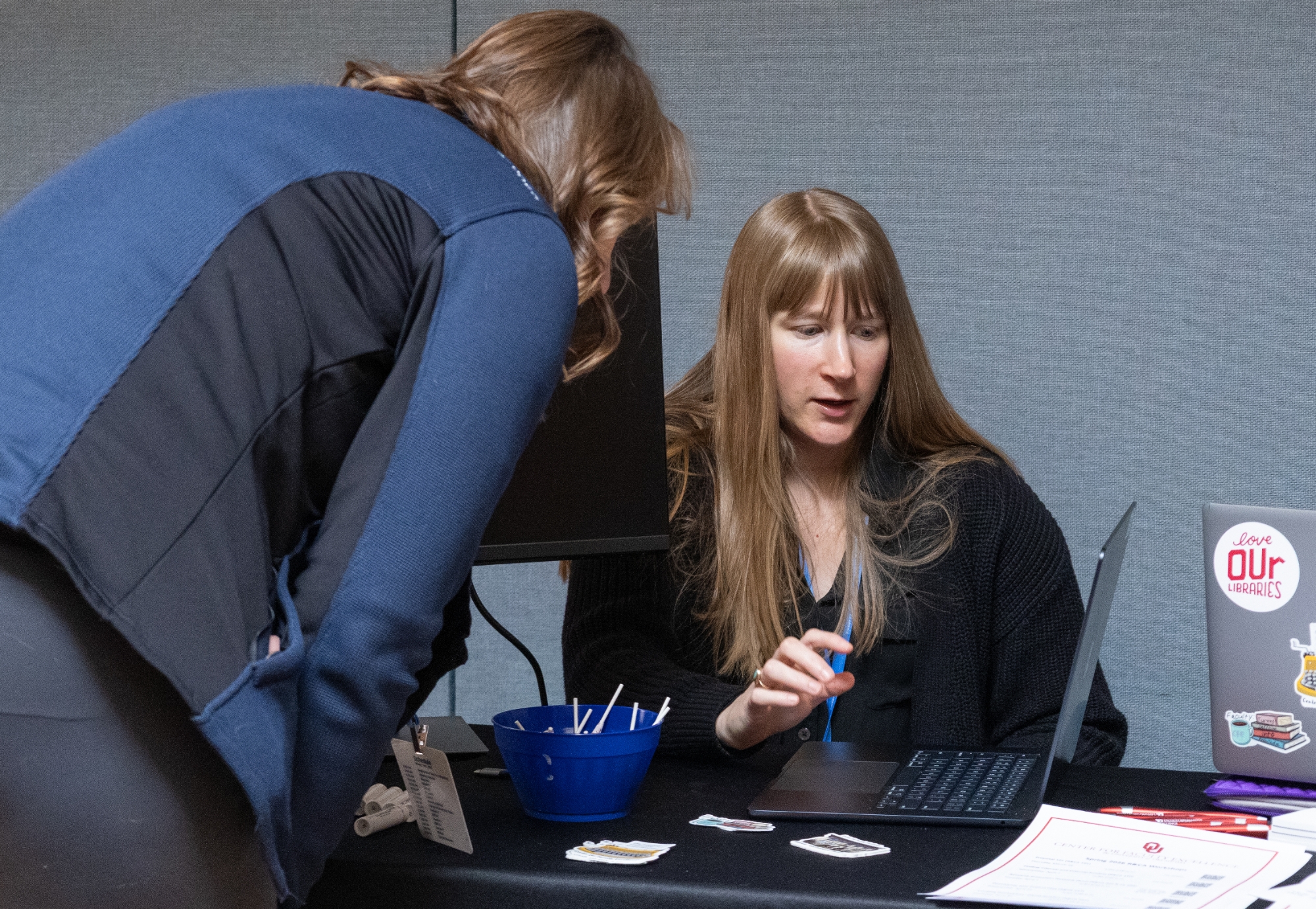 A person talking at a table showing their computer to another person.