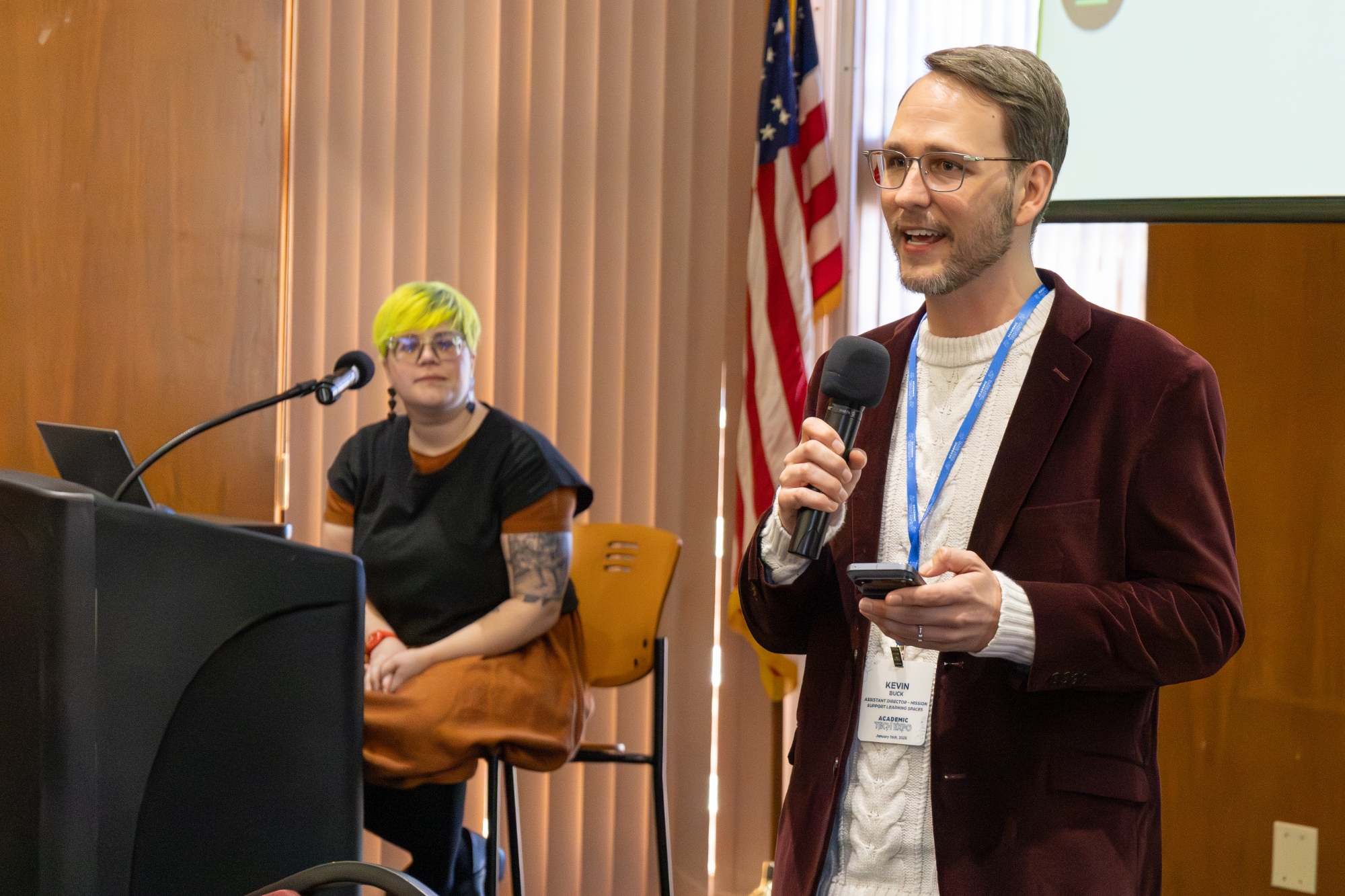 Person with a microphone introducing a person behind them speaking at a podium.