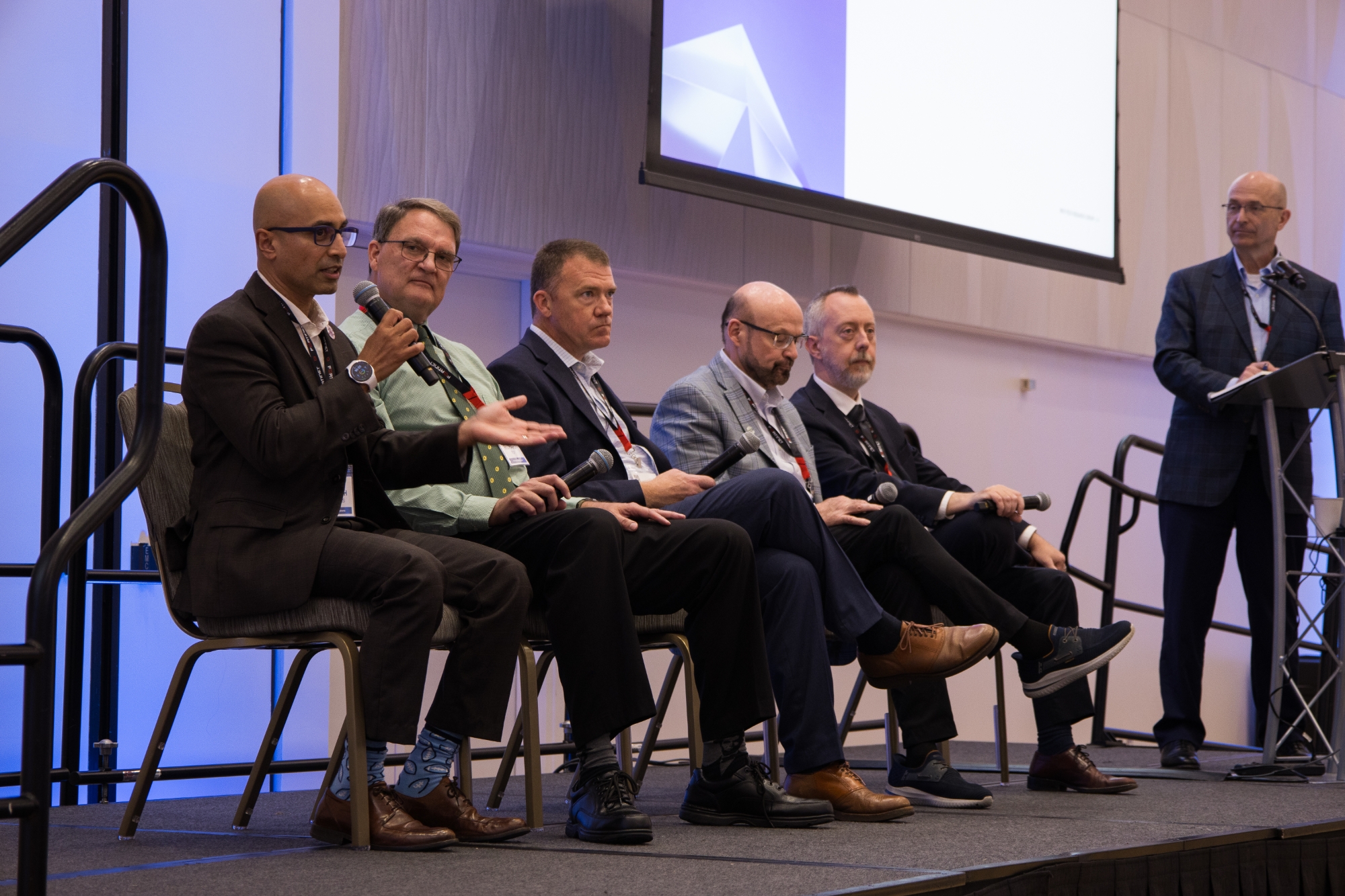 Five men on a panel and one is speaking.