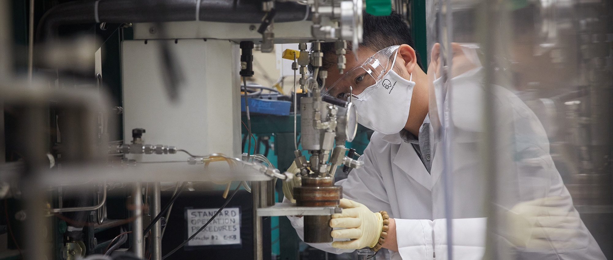An OU researcher wearing safety googles and a mask works with laboratory equipment.