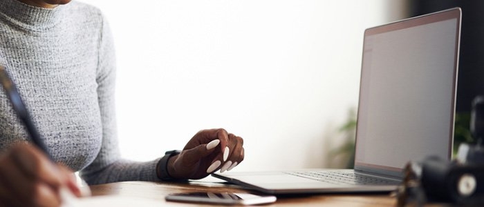 close up of a woman taking notes in a notebook with her laptop open on the desk