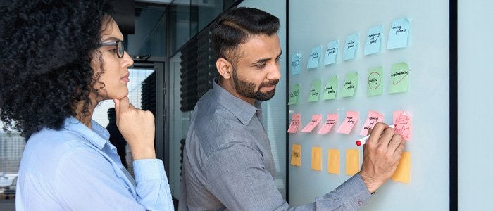 two coworkers using sticky notes on a white board to plan out a project