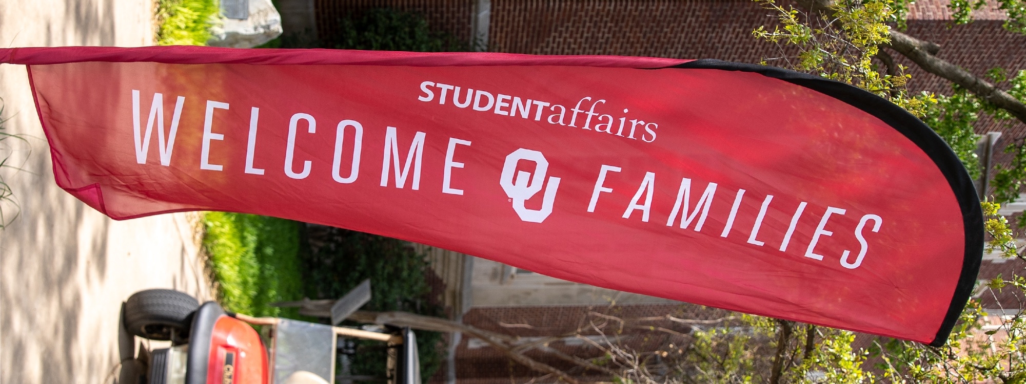 Crimson flag displaying Welcome OU Families on campus.