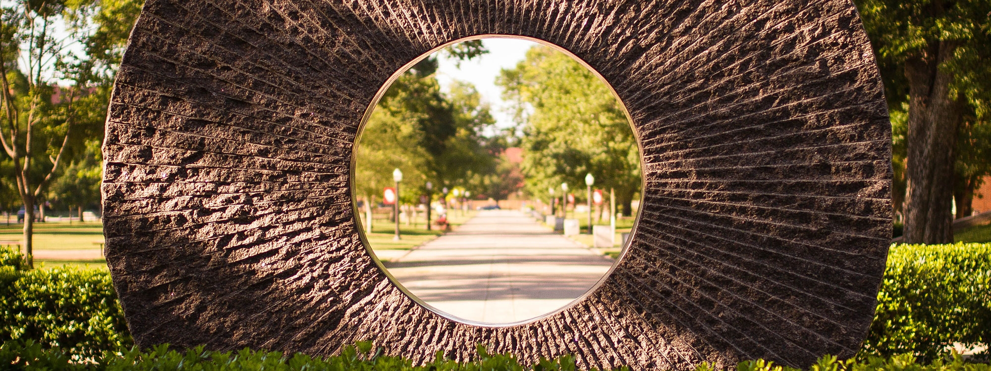 A circular stone sculpture with trees and the North Oval of campus visible through the circle.