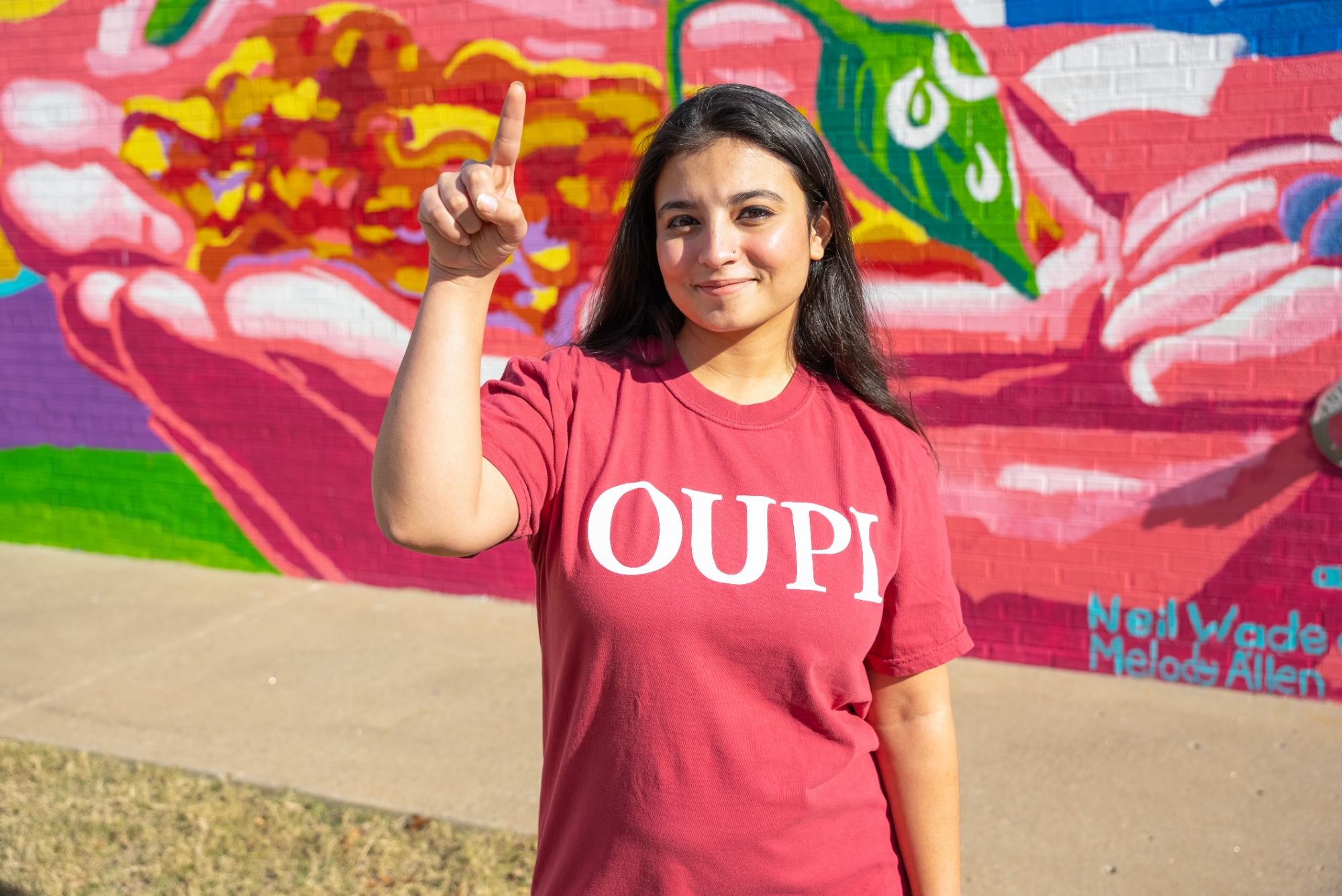 Student wearing OUPI shirt standing on campus in front of a mural.