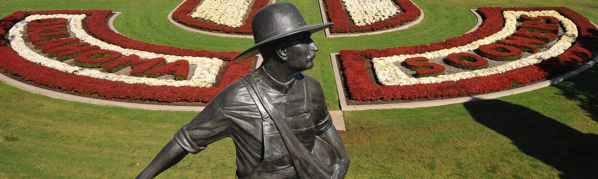 The bronze seed sower statue at the entrance of the North oval with crimson and cream mums.