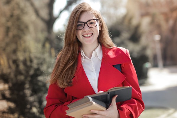 photograph of a smiling female student holding a stack of books