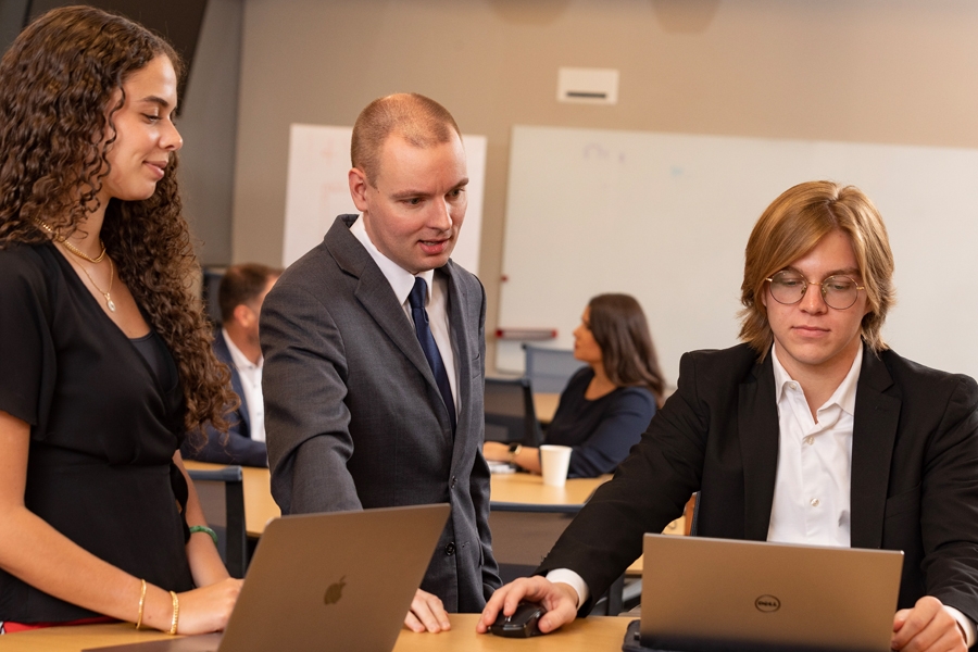 A professor sitting at a table with two students using laptops. 