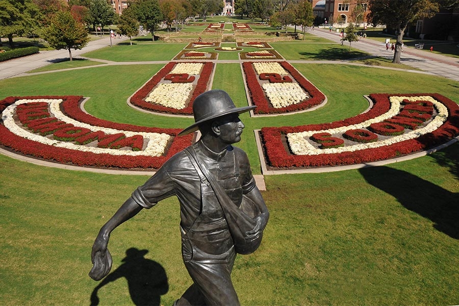 Bronze statue of the OU Seed Sower with crimson and cream mums arranged along the South Oval