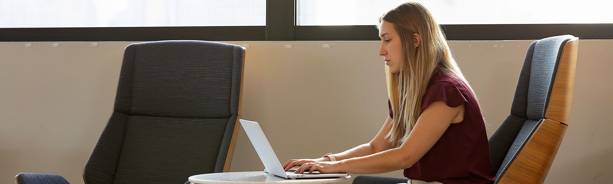 A students sitting near a window working on a laptop computer. 