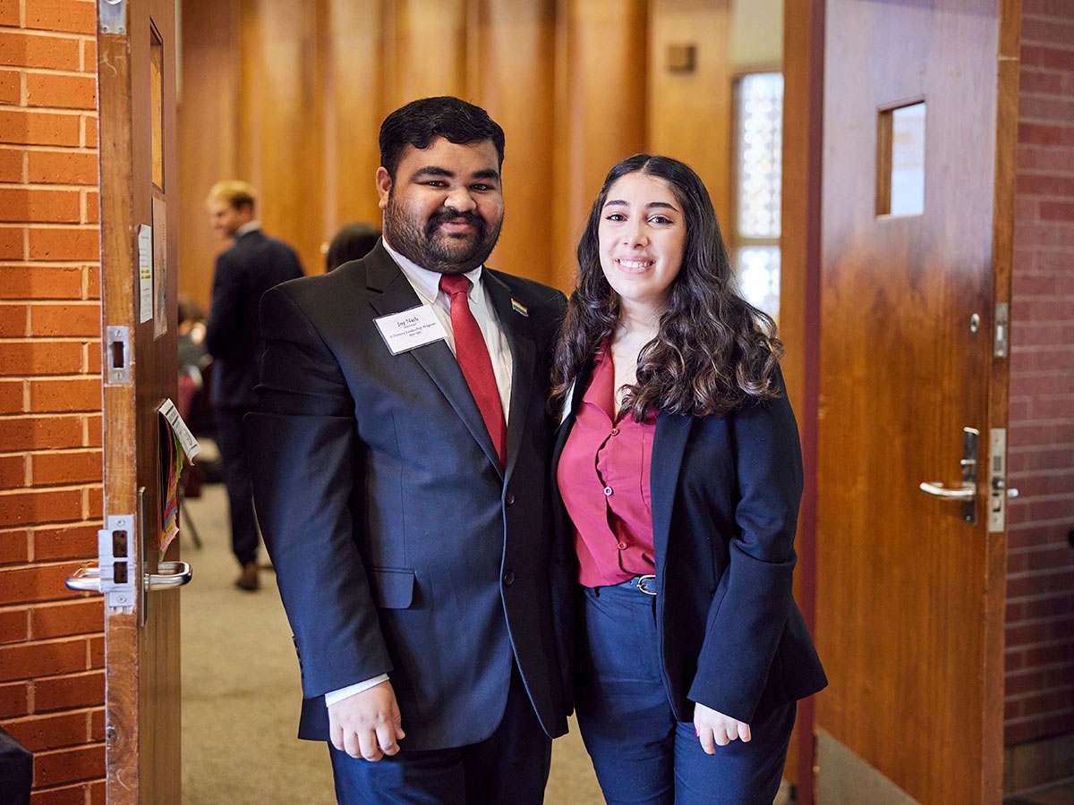 Two professionally dressed students welcome guests to the conference.