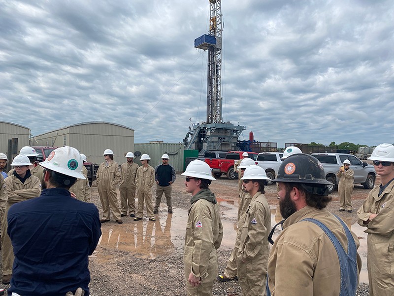 Students dressed in coveralls and hard hats visit a drilling site.