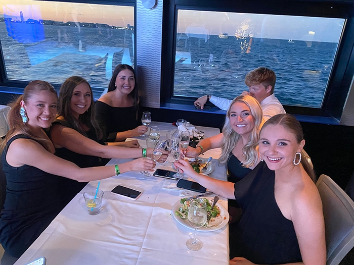 5 young women and one young man sit at a dinner table on a boat during AAPL annual gathering