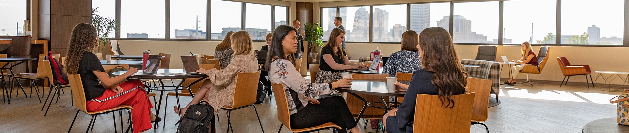 Many MBA students in small groups studying or relaxing in the Rainbolt Graduate School lounge area.