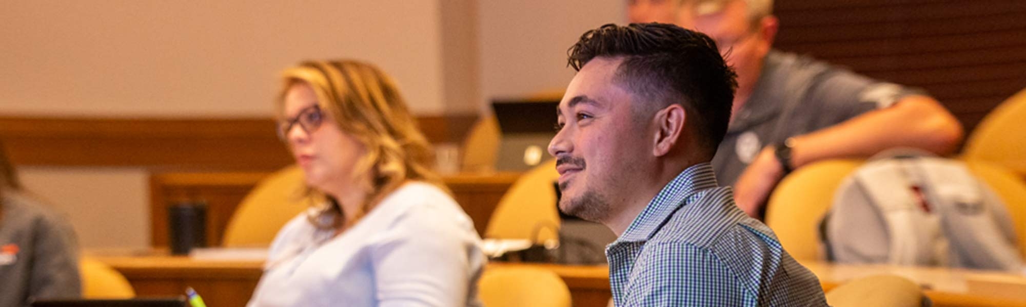 Several students sit in a lecture hall taking notes and listening to instruction.