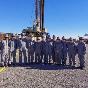 Students of the Price College Oil and Gas Accounting class pose in front of an oil rig in their safety protective gear.
