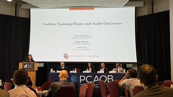 Ph.D. student Mengyang Davila stands at a podium in front of a room of people at the PCAOB conference.