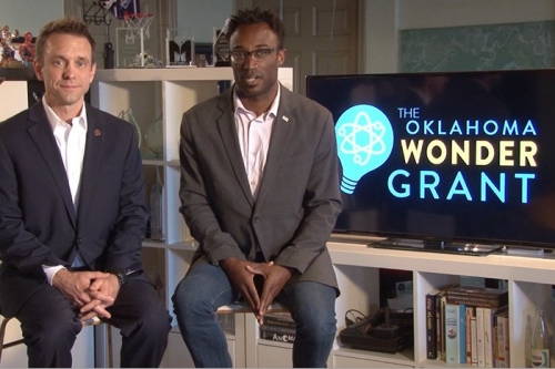 Two men sitting in front of a flat sceenadvertising the Oklahoma Wonder Grant