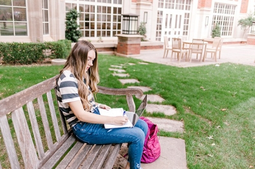 Student sitting on a bench outside of Price Hall at the University of Oklahoma