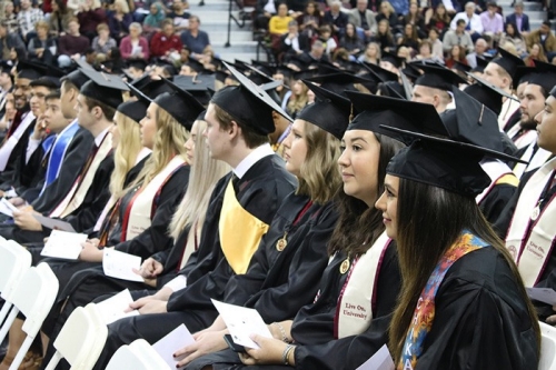 graduates in cap and gown sit at graduation ceremony