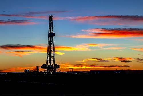 Oil drilling site silhouetted against a blue, and orange sky at sunset