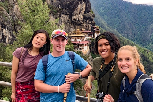 Four of Price college's undergraduates pose for a photo of their international travels in front of a forested mountain landscape