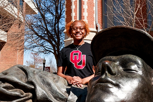 Noel Bland poses for a photo near a statue on the Norman campus at the University of Oklahoma