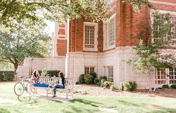Students sit on a bench outside of the Price College of Business on the University of Oklahoma campus