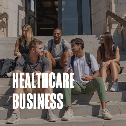 A group of students sit together on the steps of the front entrance to Adams Hall. Text over the photo reads: Healthcare Business.