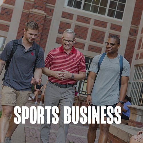Dean Corey Phelps walking with two students through Dodson Courtyard with two students. Text over the photo reads: Sports Business.