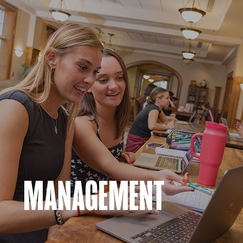 Two students sit together while working at a study table in the Price Hall lounge. Other students are visible in the background. Text over the photo reads: Management.