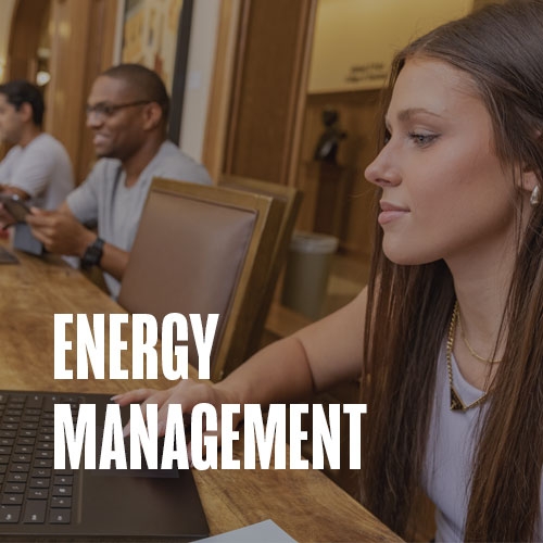 A professor assists a student in the computer lab at Price College. Text over the photo reads: Energy Management