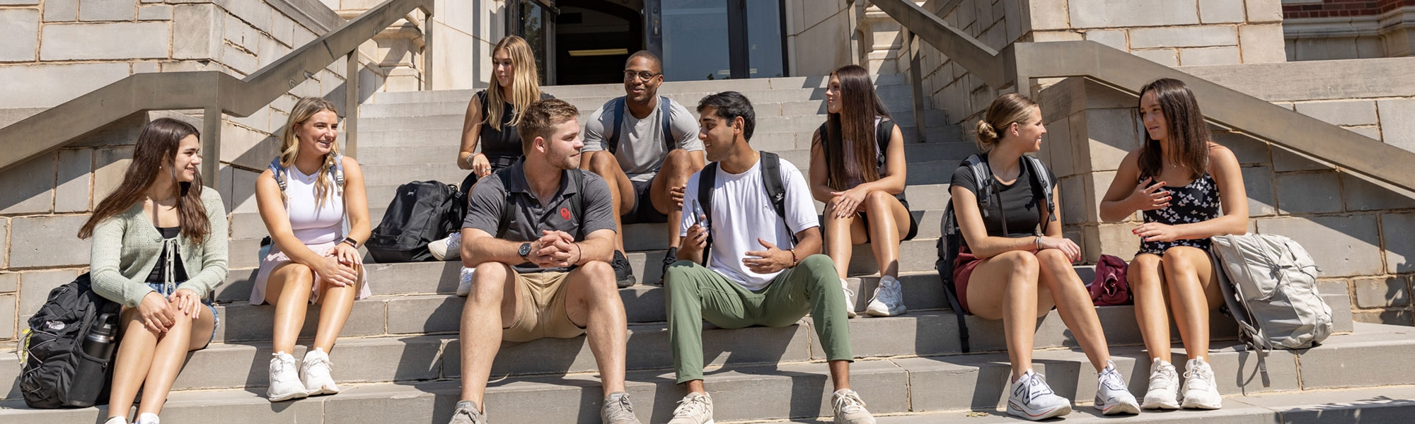 A large group of students sitting on the steps that lead to the entrance of Adams Hall.