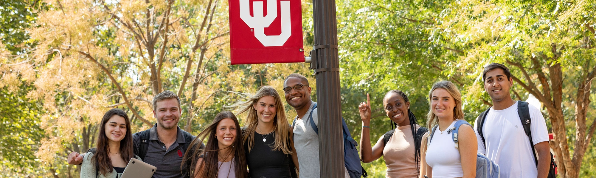 A large group of students standing near an OU lamppost on campus.