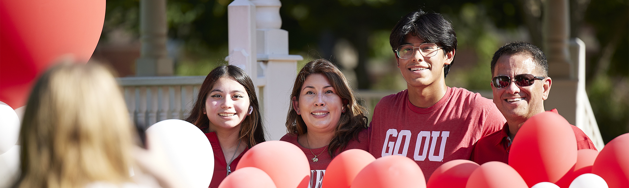 A family of four wearing OU shirts and surrounded by balloons poses for a photo at the University of Oklahoma.
