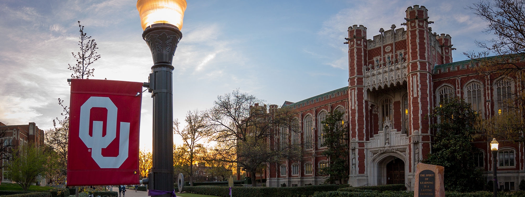 An O U flag on a lamppost in front of Bizzell Memorial Library.