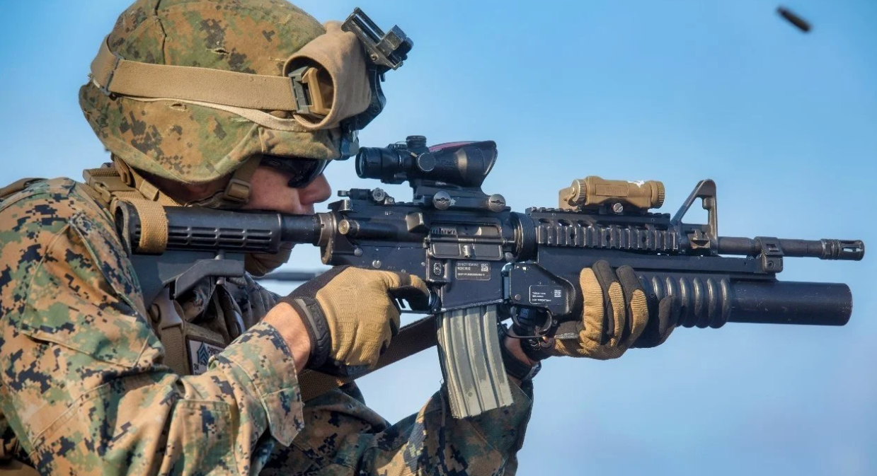 Military personnel look down the scope of their rifle.