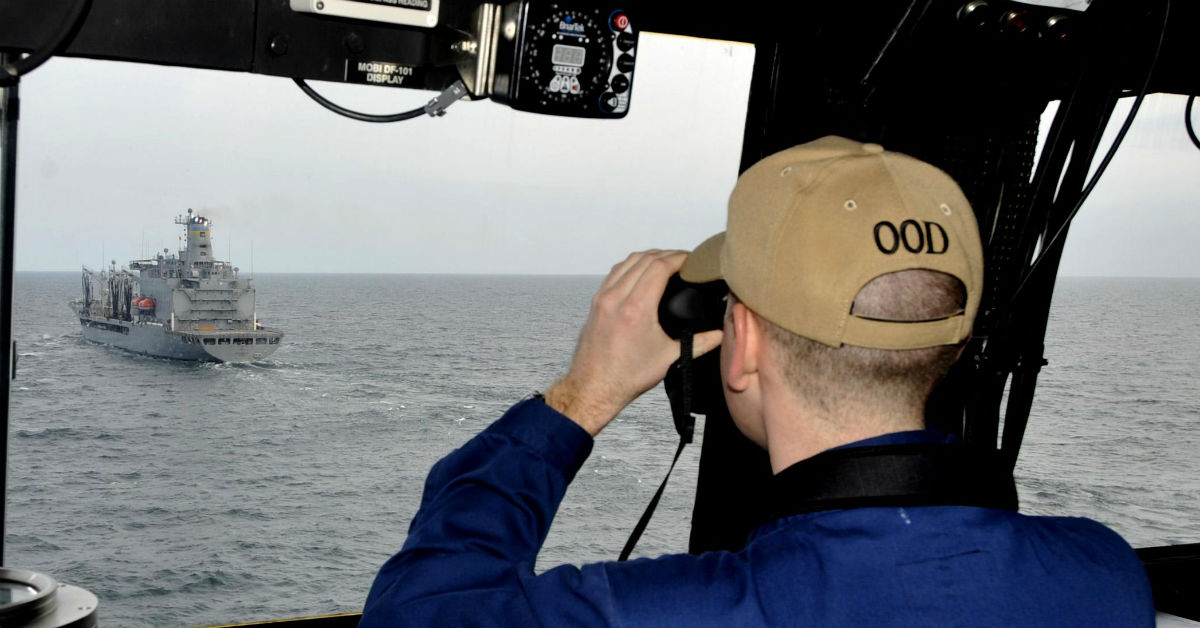 Naval officer looking at another ship through a pair of binoculars.