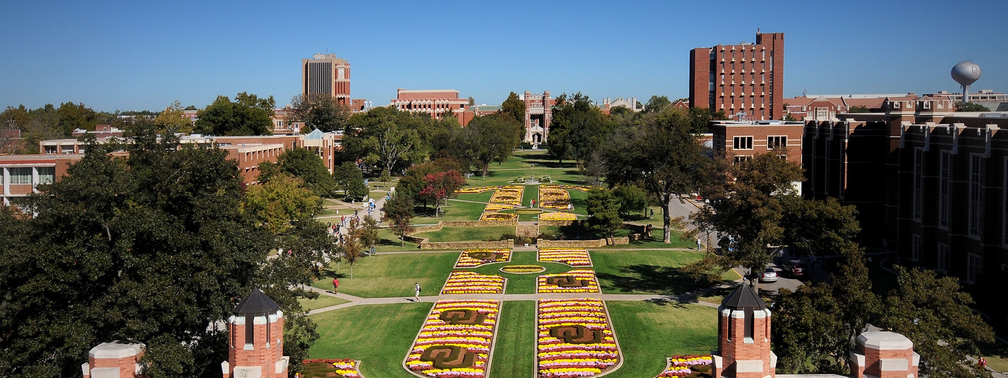 A large outdoor quad area with colorful flowers and buildings on right and left side.