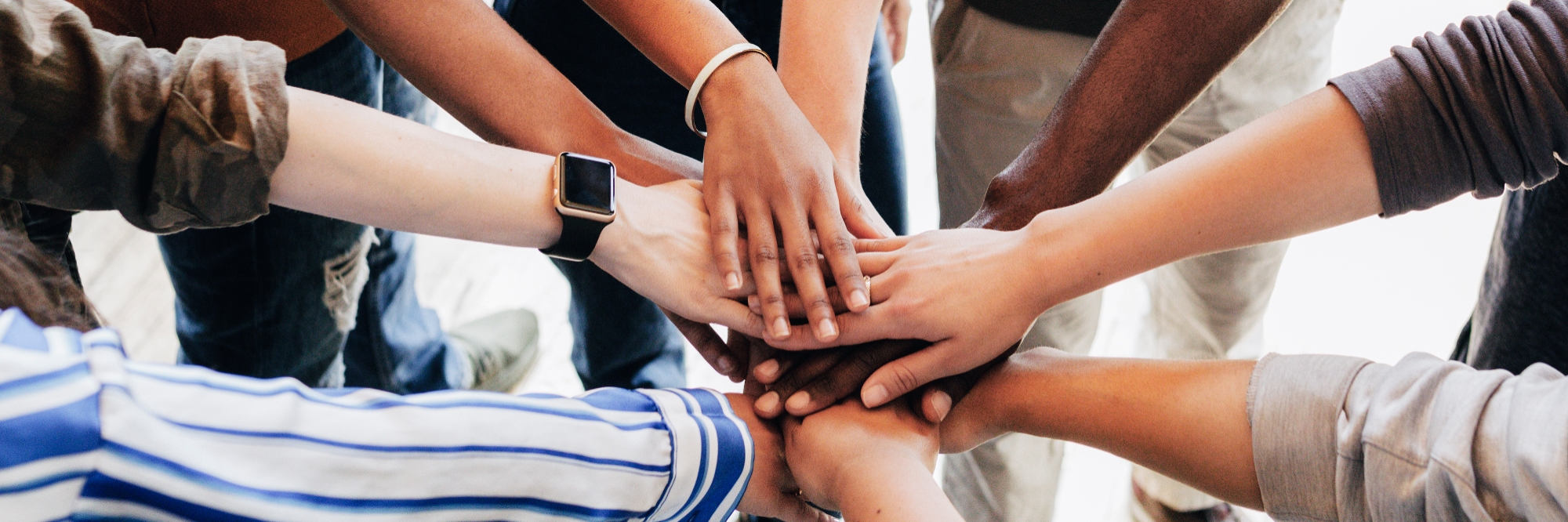 A close up shot of people standing in a circle with their hands stacked in the middle.