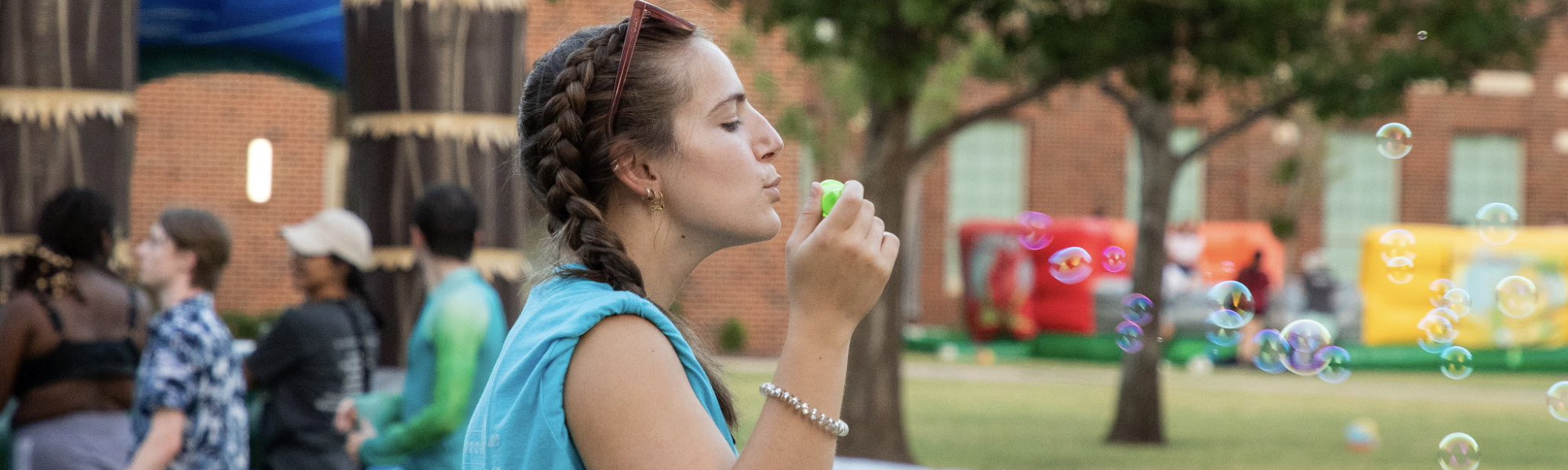 A student blowing bubbles at a summertime event.