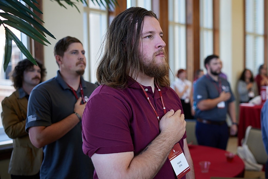 Attendees of the 2024 MVC Reception salute the flag during the National Anthem before the event.